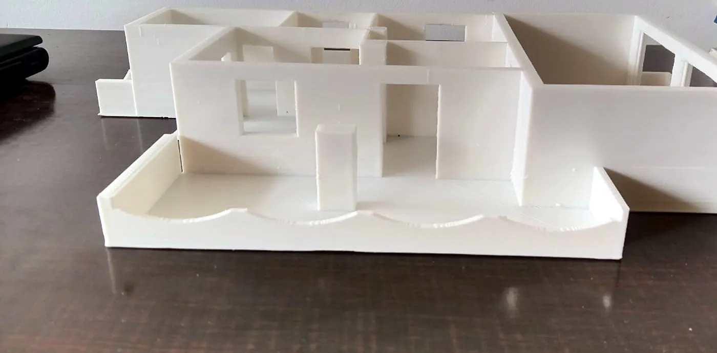 White 3D-printed architectural floor-plan model of a house seen from the side, showing walls, doors and windows