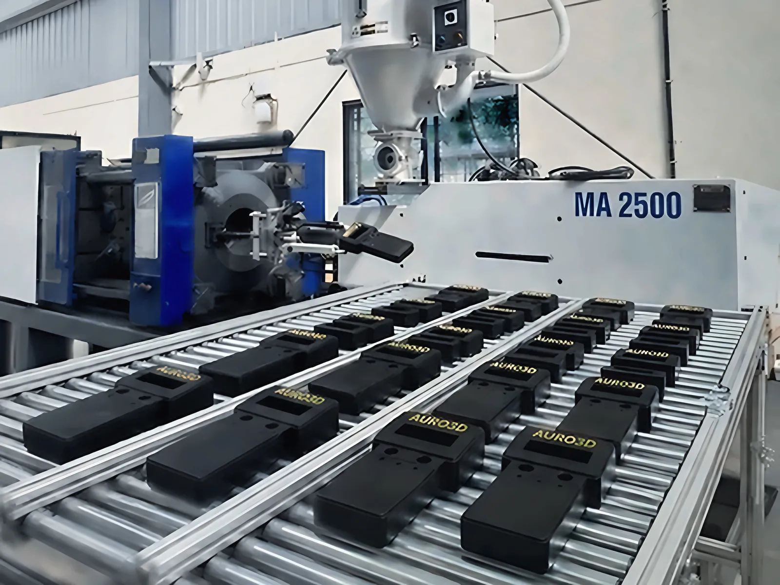 Black injection-moulded parts on a conveyor next to the Haitian MA 2500 press