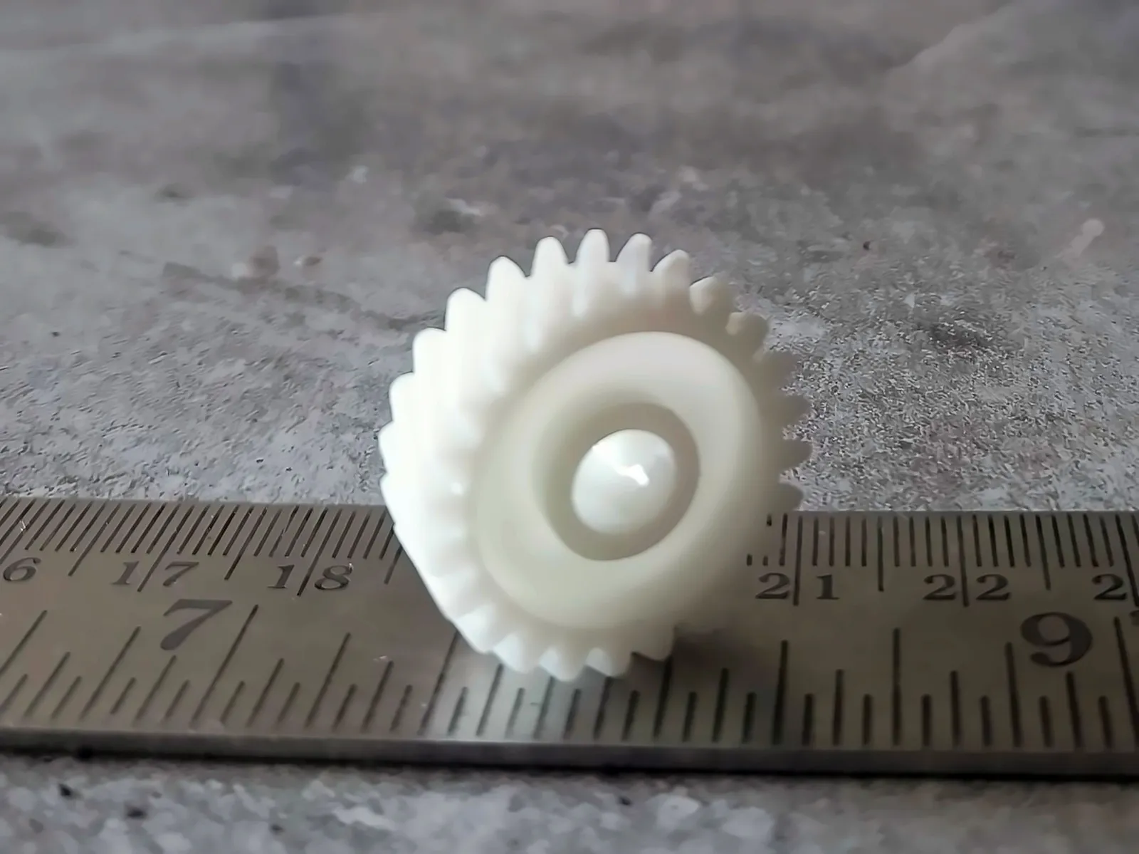 Small white resin-printed gear next to a steel ruler for scale