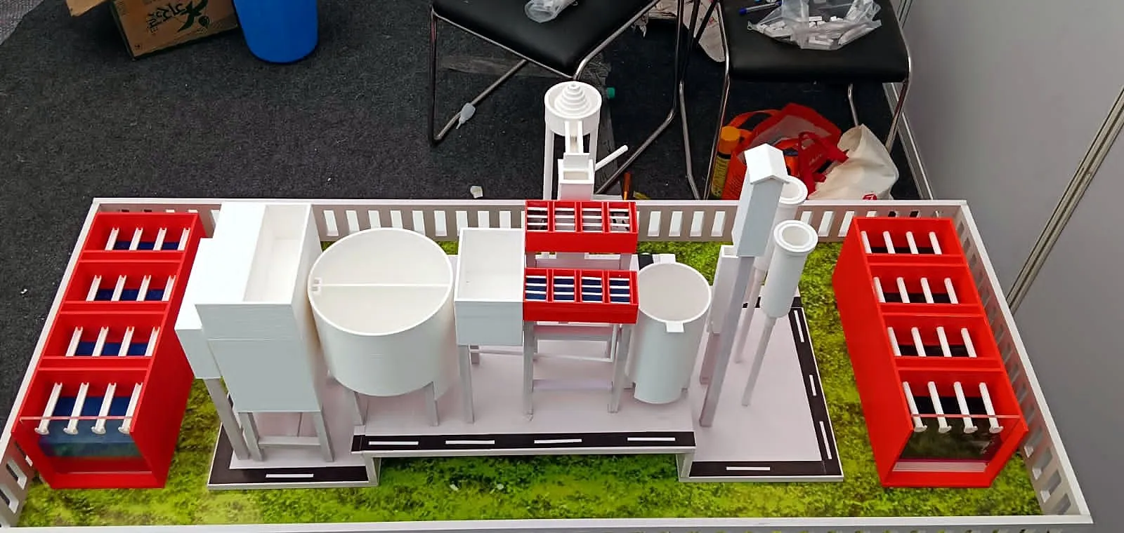 3D-printed treatment plant model showing red filter-bed blocks, circular tanks and piping on a landscaped base
