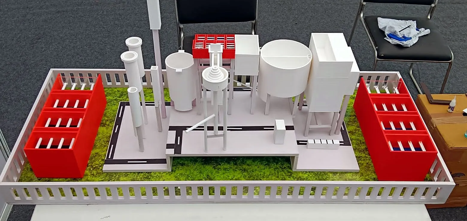 Front view of a 3D-printed 100 MLD water treatment plant model with red filter beds, tanks and towers inside a white fence